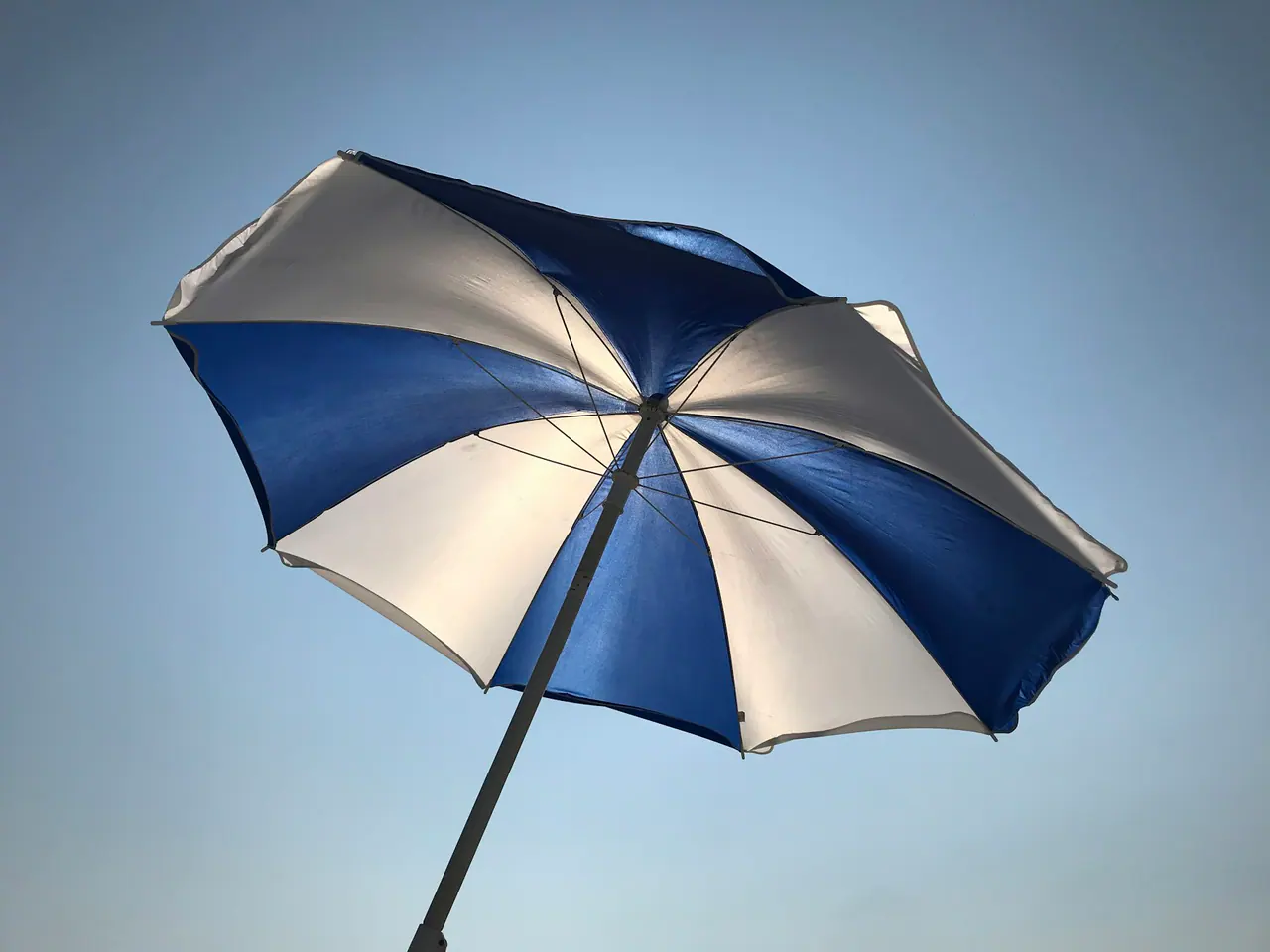 Blue and white cantilever umbrella against a clear sky